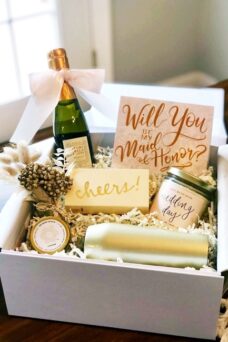 Geschenkbox mit verschiedenen Kleinigkeiten wie eine kleine Sektflasche, Seife und eine Karte mit dem Schriftzug "Will you be my maid of honor?"